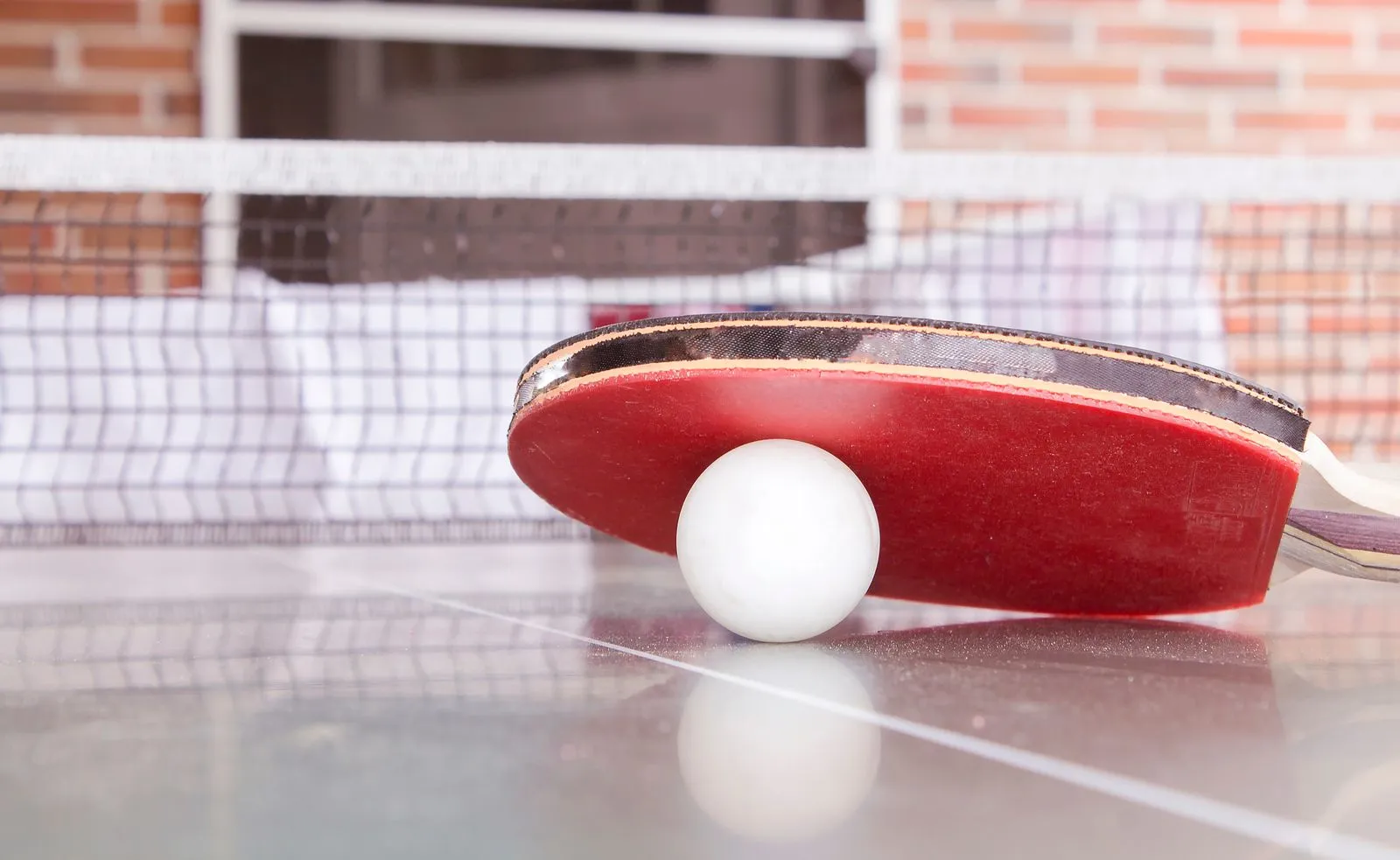 Table tennis ball resting on a net cord between two tables
