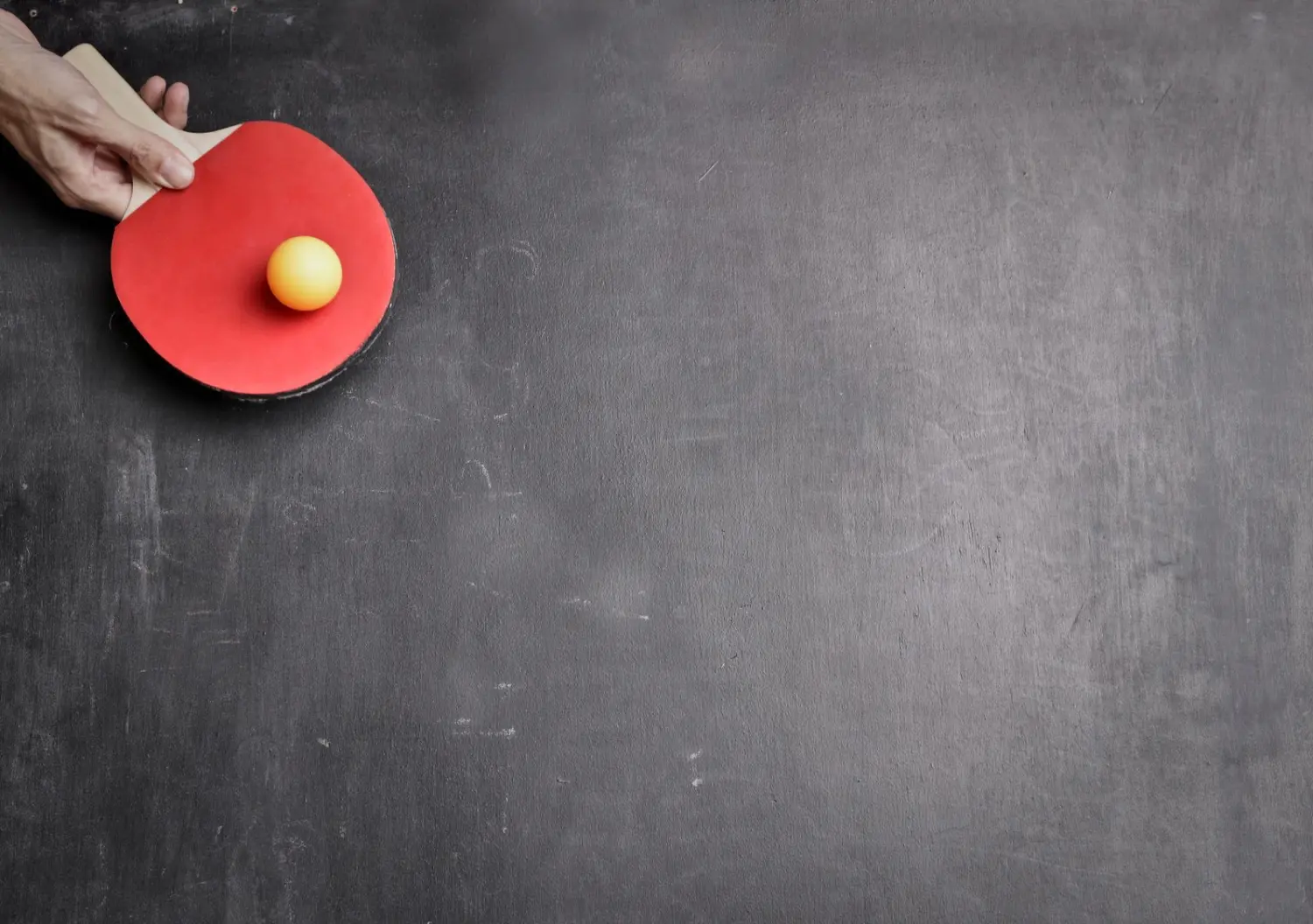 A hand holding a red table tennis paddle, poised over the table